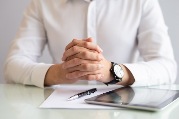 Primer plano de ejecutivo masculino sentado en la mesa con las manos juntas