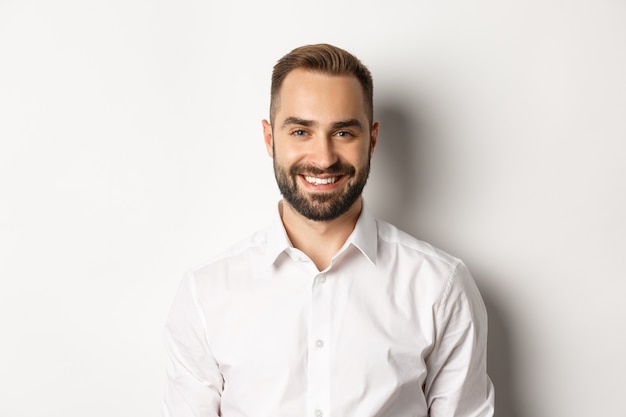 Primer plano de empleado de sexo masculino confiado en camisa de cuello blanco sonriendo a la cámara, de pie seguro de sí mismo contra el fondo del estudio.