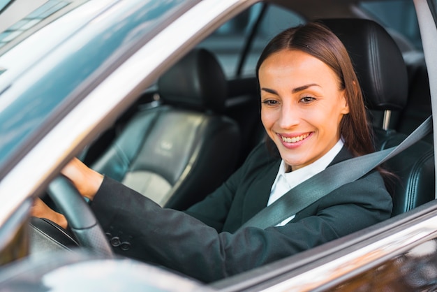 Primer plano de una empresaria joven sonriente conduciendo un coche