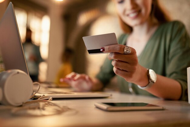 Primer plano de una empresaria que usa una computadora portátil y una tarjeta de crédito para comprar en línea mientras trabaja hasta tarde en la oficina