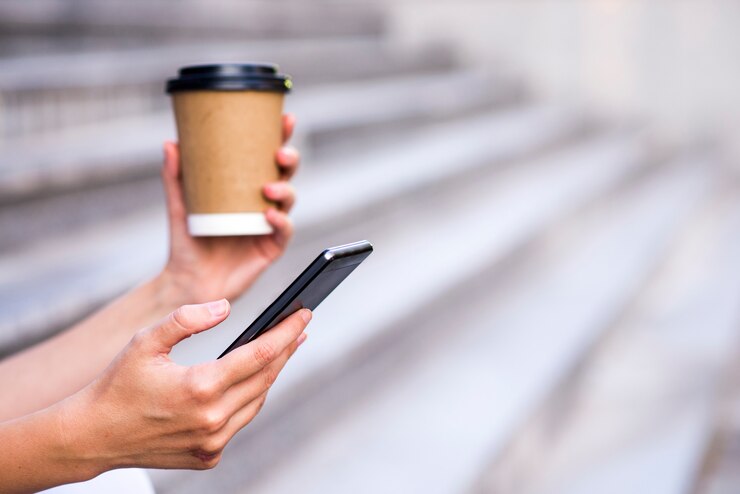Primer plano de una empresaria utilizando teléfono móvil y celebración taza de papel. Close-up detalle de una mano de negocios la celebración de taza de papel y el uso de un teléfono inteligente