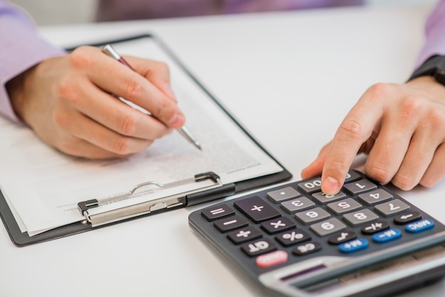 Primer plano del empresario calculando facturas utilizando calculadora