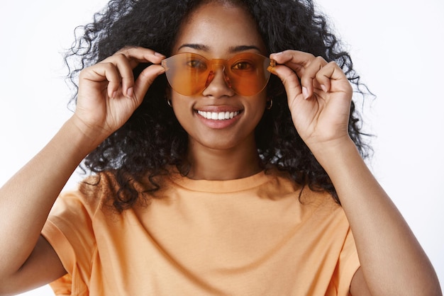 Primer plano encantador sonriente niña afroamericana peinado afro comprobando gafas de sol bying nuevo par gafas prepárate turista viajes vacaciones sonriendo encantado recogiendo gafas tienda fondo blanco