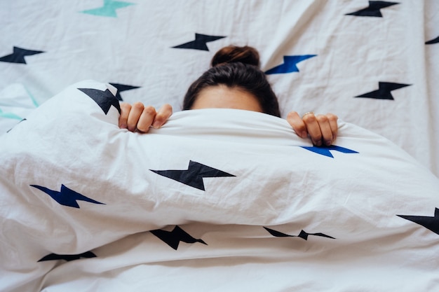 Primer plano de encantadora joven se encuentra en la cama cubierta con una manta.