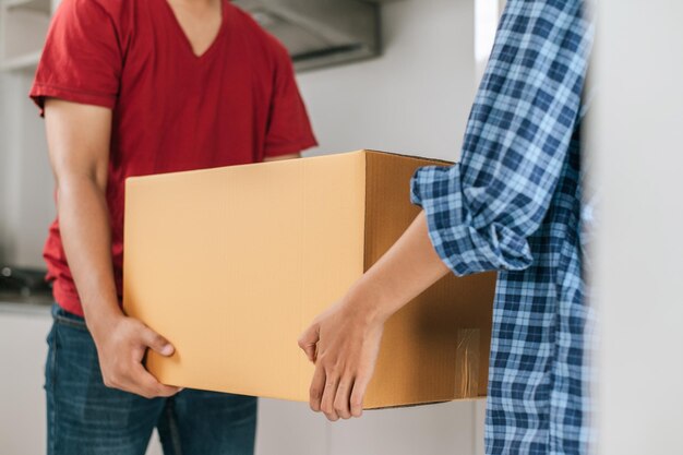 Primer plano Enfoque selectivo Pareja joven asiática ayuda a sostener una caja de cartón pesada caminar hacia una nueva casa con felicidad nuevo concepto de mudanza de casa