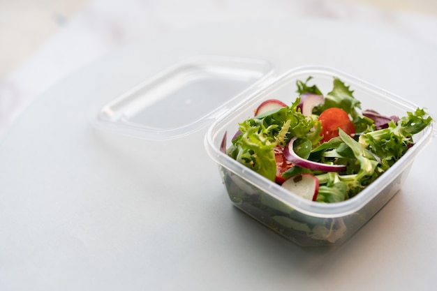 Primer plano de ensalada fresca en una caja de plástico sobre una superficie blanca