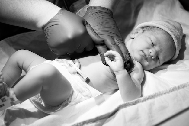 Primer plano en escala de grises de un médico que controla a un niño recién nacido bajo las luces en un hospital