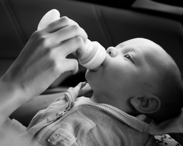 Primer plano en escala de grises de una persona que alimenta a un niño recién nacido bajo las luces con un fondo borroso
