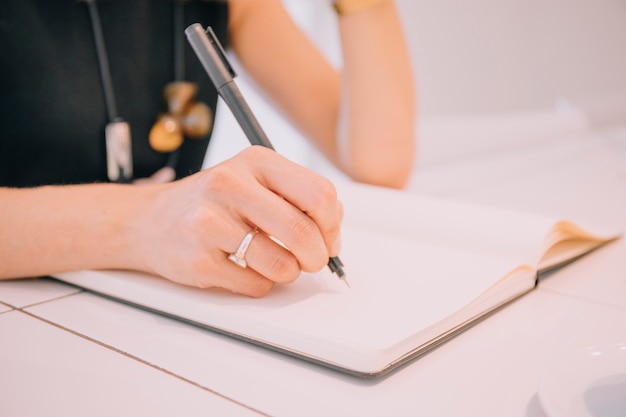 Primer plano de la escritura de la mano de la empresaria con la pluma en el diario