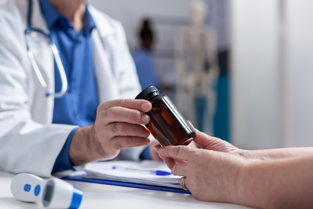 Primer plano de un especialista que le da una botella de pastillas a una anciana en la visita de control anual. Manos de médico sosteniendo un frasco con medicamentos recetados y tratamiento para ayudar a curar enfermedades. remedio medico