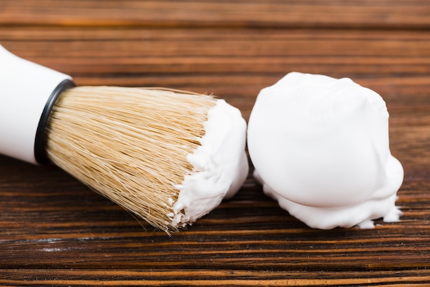 Primer plano de espuma de afeitar con pincel en escritorio de madera