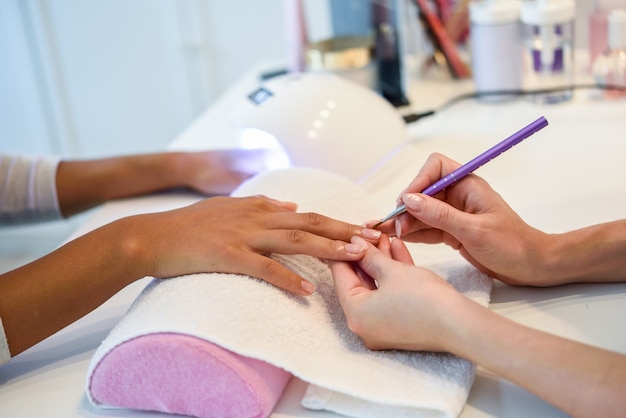 Primer plano de esteticista pintando las uñas de una mujer con un pincel en un salón de uñas