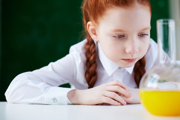 Primer plano de estudiante analizando el matraz con líquido naranja