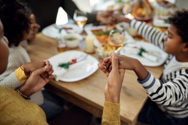 Primer plano de una familia afroamericana diciendo gracias antes de la comida de Navidad en el comedor