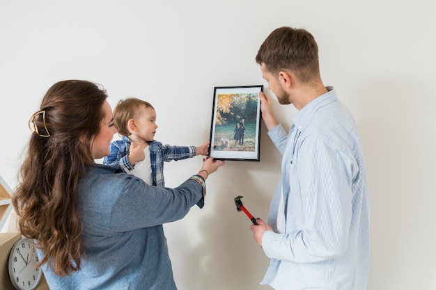 Primer plano de la familia feliz con marco de foto contra la pared en el nuevo hogar