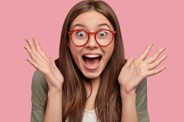 Primer plano de feliz estudiante asombrado posando contra la pared rosa