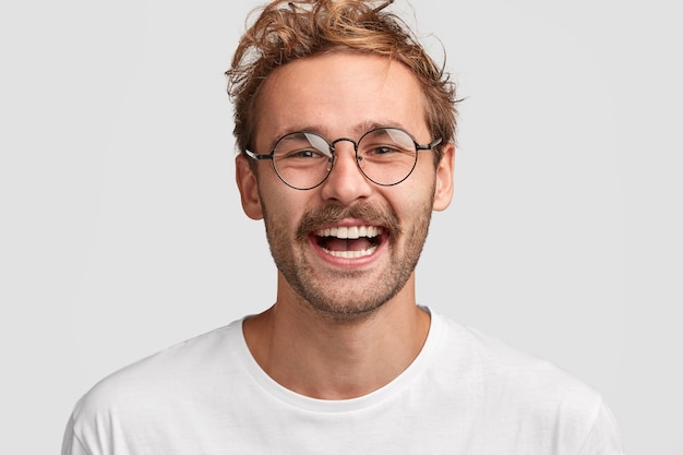 Primer plano de feliz hombre elegante con gafas redondas, tiene una sonrisa positiva en la cara, me alegra recibir un salario, gastar dinero en nuevas compras