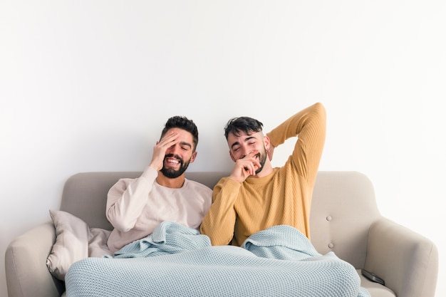Primer plano de la feliz pareja gay sentada en el sofá junto con una manta sobre fondo blanco