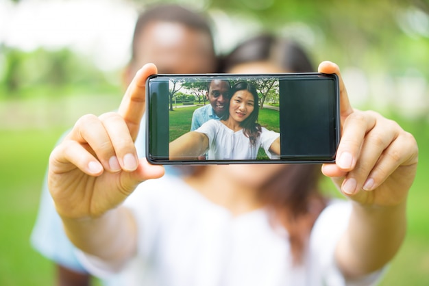 Primer plano de la feliz pareja multiétnica fotografiando a sí mismos en el teléfono inteligente