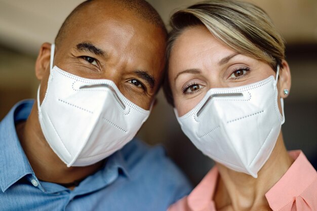 Primer plano de una feliz pareja multiétnica con mascarillas protectoras mirando a la cámara