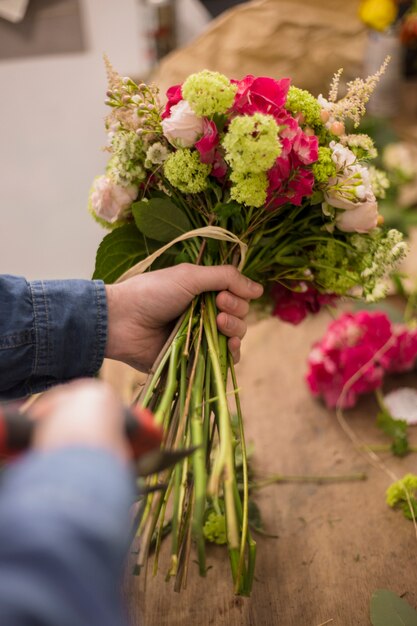 Primer plano de un florista masculino cortando el tallo del ramo con tijeras de podar