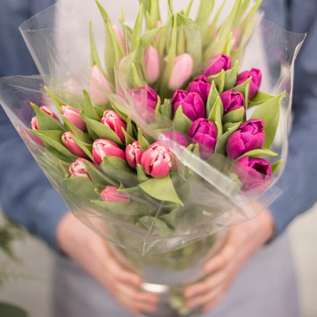 Primer plano de un florista masculino con ramo de flores de tulipán rosa