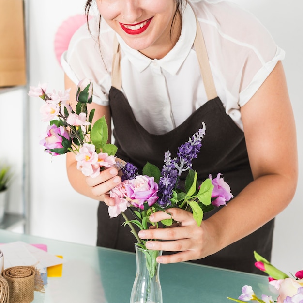 Foto gratuita primer plano de una floristería femenina poniendo flores en el florero en el escritorio de vidrio