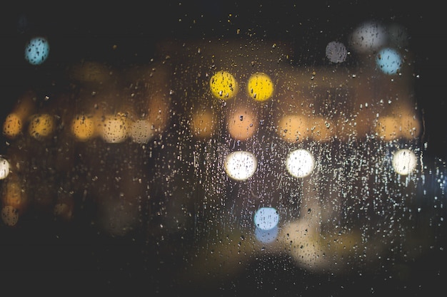 Primer plano de gotas de lluvia en una ventana de cristal transparente con luces borrosas