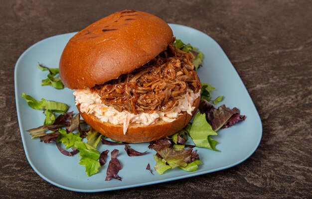 Primer plano de una hamburguesa de carne tirada jugosa abierta rodeada de verduras en una placa azul