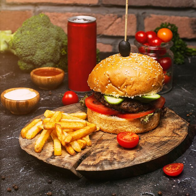 Primer plano de hamburguesa casera con carne de res, tomate, lechuga, queso y papas fritas en tabla de cortar. Comida rápida