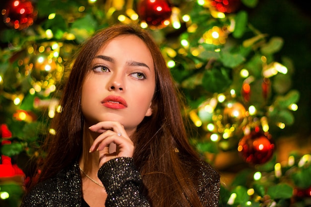 Primer plano de una hermosa joven delante de un árbol de Navidad