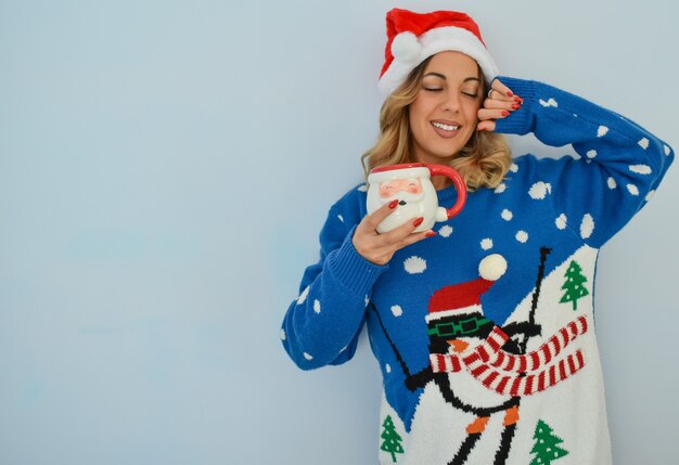 Primer plano de una hermosa joven con un vestido de Navidad y un sombrero sosteniendo una taza de Santa