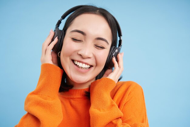 Primer plano de una hermosa mujer asiática en auriculares sonríe y escucha música disfruta de soportes de podcast