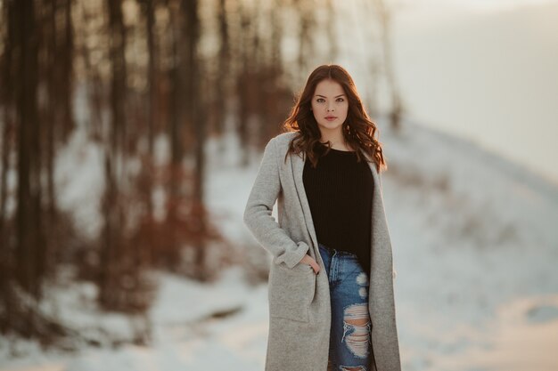 Primer plano de una hermosa mujer con cabello rubio y una chaqueta gris en el parque cubierto de nieve