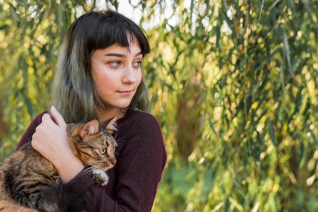 Primer plano de una hermosa mujer sonriente abrazando a su gato atigrado en el parque