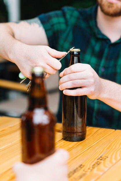 Primer plano del hombre abriendo la botella con el abrelatas en la mesa de madera