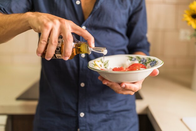 Primer plano, de, hombre, aderezo, el, ensalada, con, aceite de oliva, en, el, tazón