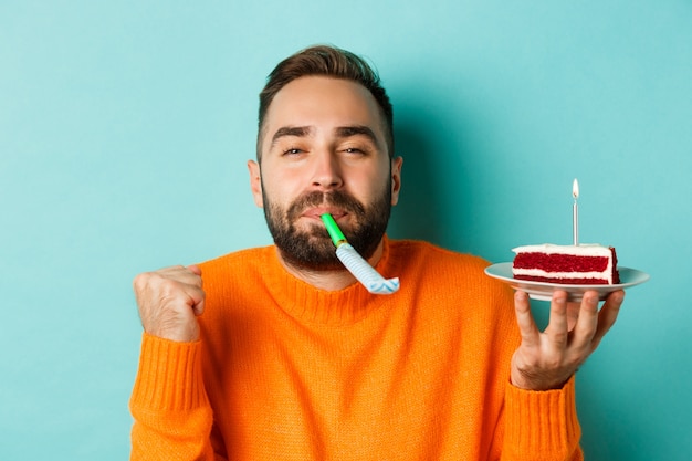 Primer plano de hombre adulto divertido celebrando su cumpleaños, sosteniendo el pastel de cumpleaños con vela