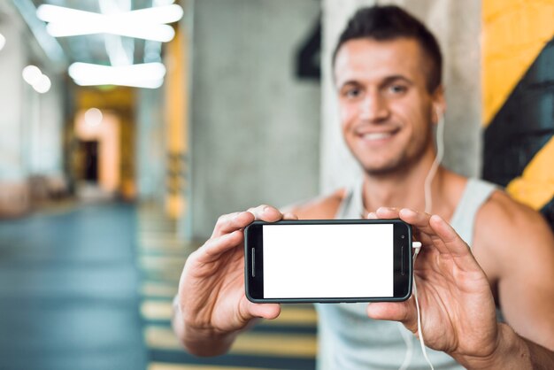 Primer plano de un hombre atlético que muestra el teléfono móvil con pantalla en blanco en blanco