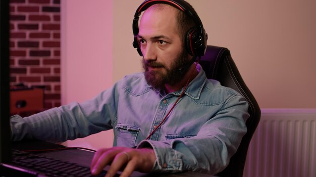 Primer plano de un hombre con auriculares para juegos jugando juegos de acción en línea multijugador jugando en una configuración de PC profesional. Jugador mirando la pantalla de la computadora mientras habla con los miembros del equipo en el torneo.