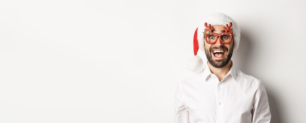 Primer plano de hombre barbudo emocionado en gafas de navidad y sombrero de santa mirando asombrado por la oferta promocional wint