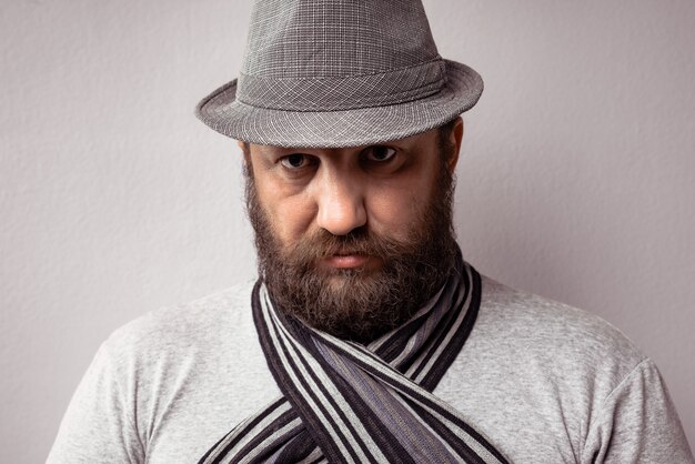 Primer plano de un hombre barbudo que llevaba una camiseta gris claro, sombrero y bufanda sobre un fondo gris