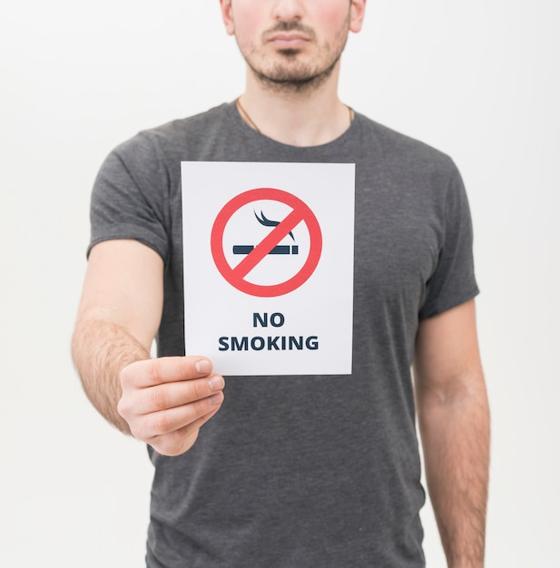 Primer plano del hombre en camiseta gris que muestra señal de no fumar sobre fondo blanco