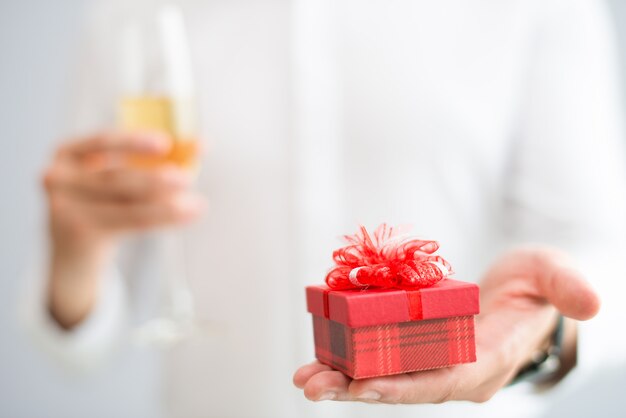 Primer plano del hombre dando una pequeña caja de regalo y sosteniendo el vaso