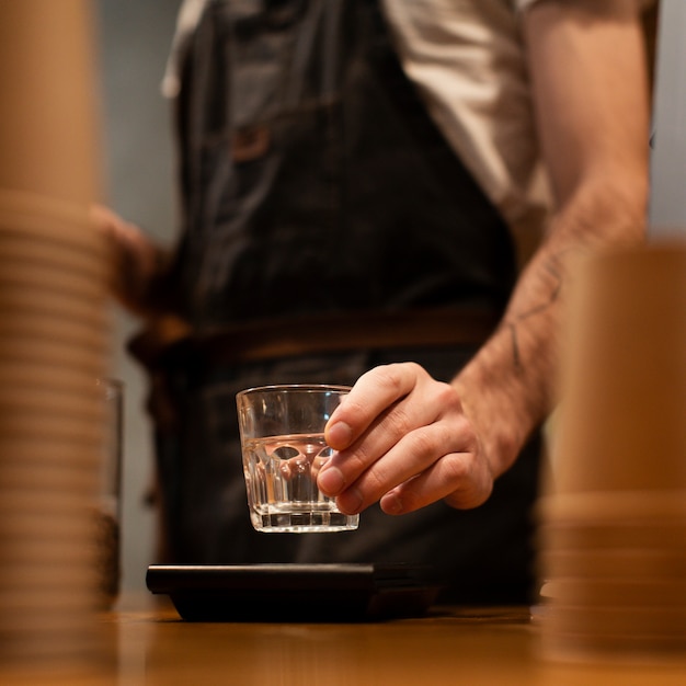 Primer plano del hombre con delantal sosteniendo un vaso transparente