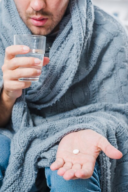 Primer plano de un hombre enfermo que muestra la píldora blanca en su mano y que sostiene un vaso de agua
