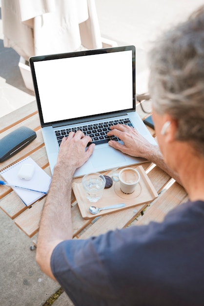 Foto gratuita primer plano del hombre escribiendo en la computadora portátil con café y vaso de agua en la mesa de madera