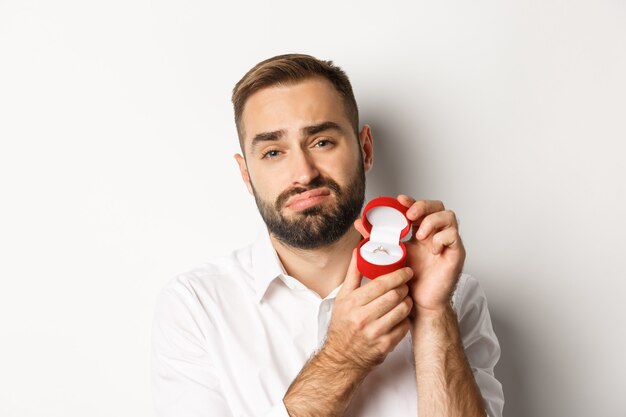 Primer plano de hombre esperanzado rogando casarse con él, con cara de tristeza y mostrando el anillo de bodas, haciendo una propuesta