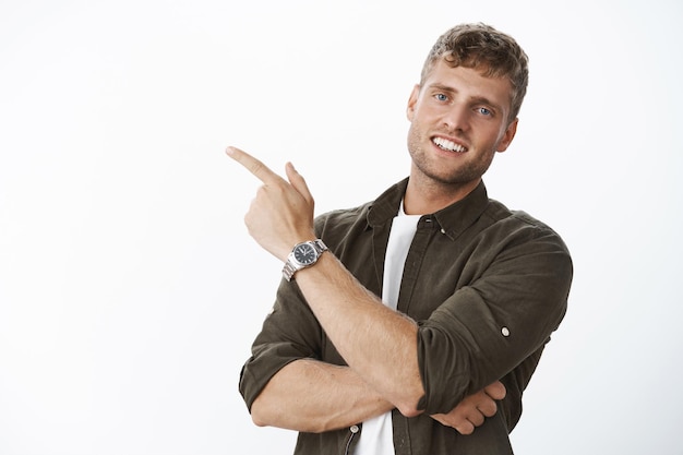 Primer plano de un hombre europeo amable y guapo con cabello rubio y sonrisa blanca apuntando a la esquina superior izquierda