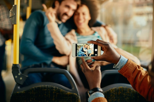 Primer plano de un hombre fotografiando a una pareja feliz con un teléfono celular en un autobús